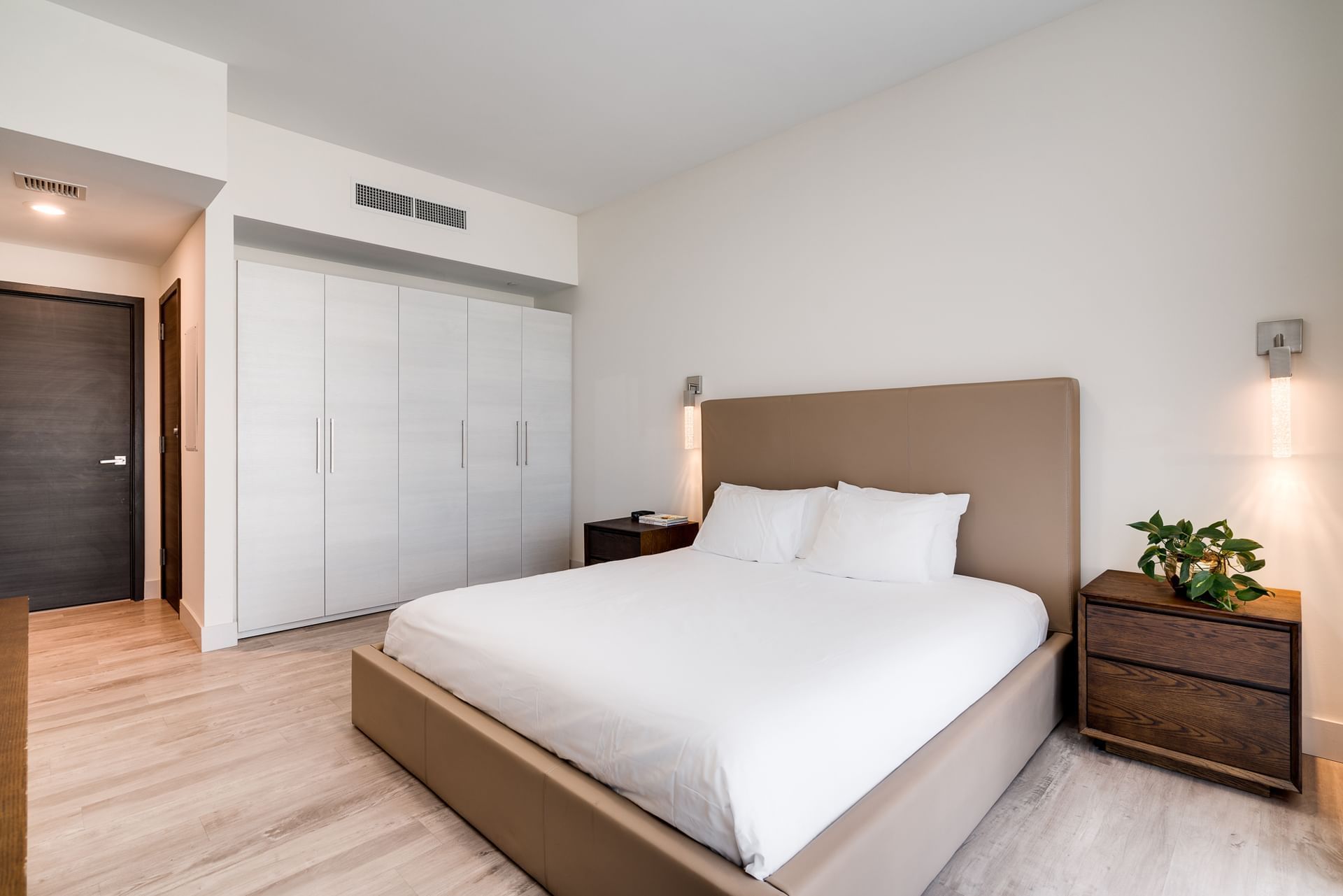 A clean and modern guest room with a large bed, wood nightstand, and white closet