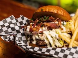Gourmet burger topped with bacon, coleslaw, and sauce served with fries in checkered basket at The Burger Dive