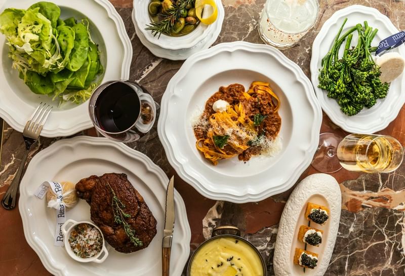 Elegant dining spread at Remi in Granduca Houston featuring steak, pasta, fresh salad, and seasonal vegetables
