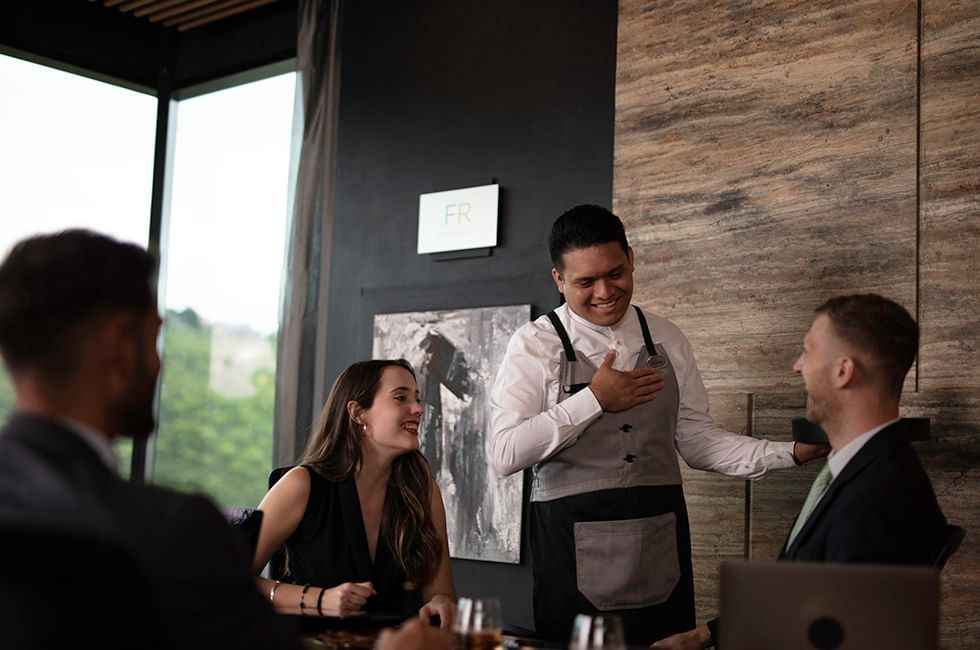 Waiter talking to two people at a dining table in restaurant at Live Aqua Resorts and Residence Club