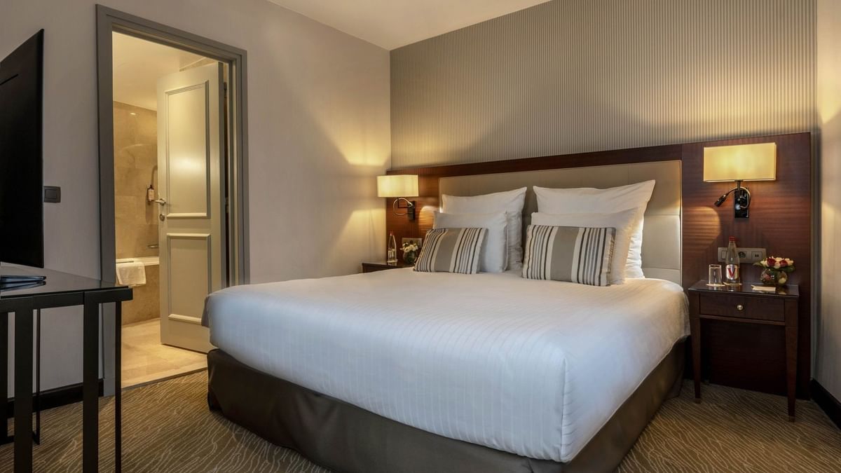 Bed between the side tables near the doorway to the bathroom in Junior Suite Privilege View at Warwick Grand Place Brussels