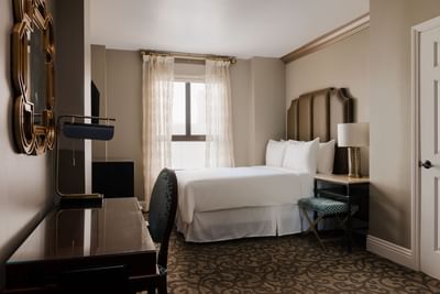 Nightstand and workspace by the cozy bed in ADA Compliant Queen Room with Roll-In Shower and carpeted floors at Hotel Bijou