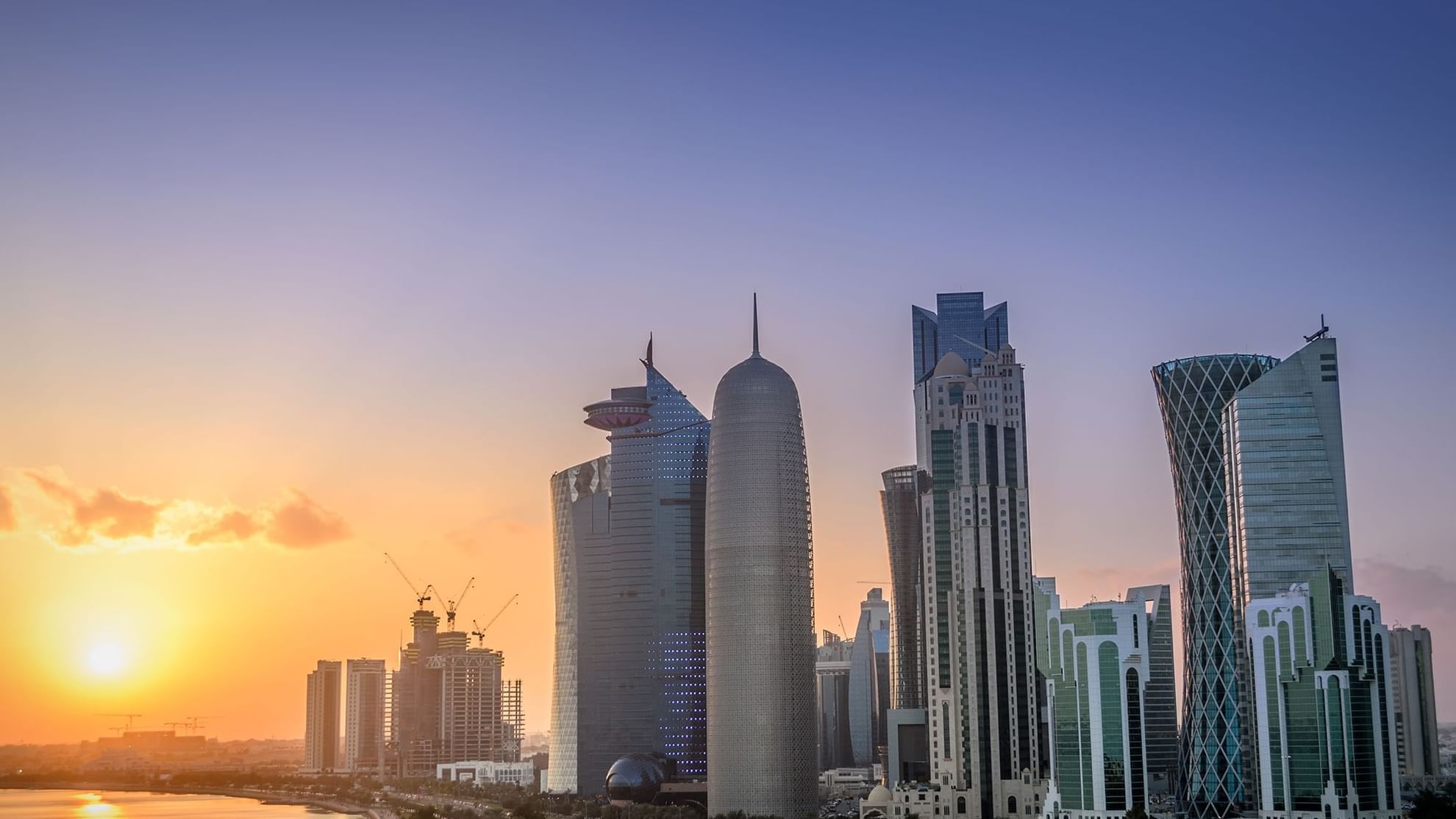 Doha skyline showcases distinctive skyscrapers, with cranes indicating ongoing construction near Warwick Hotels and Resorts