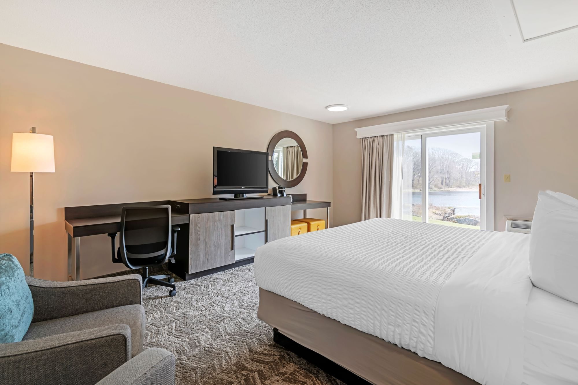 A hotel room with a large bed, desk, TV, and window