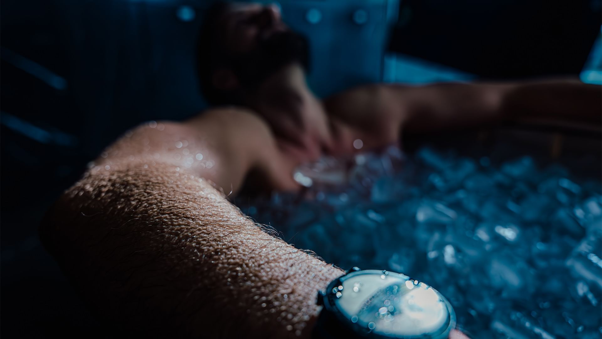 Uomo rilassato in una vasca idromassaggio, con un orologio da polso, immerso in acqua blu.