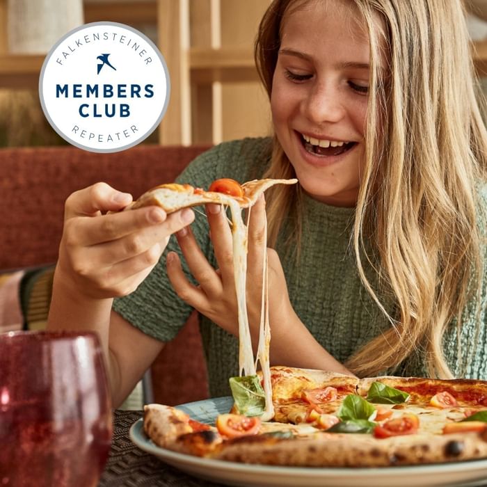 Djevojka se radosno smije dok uživa u pizzi s rastopljenim sirom u Falkensteiner Group