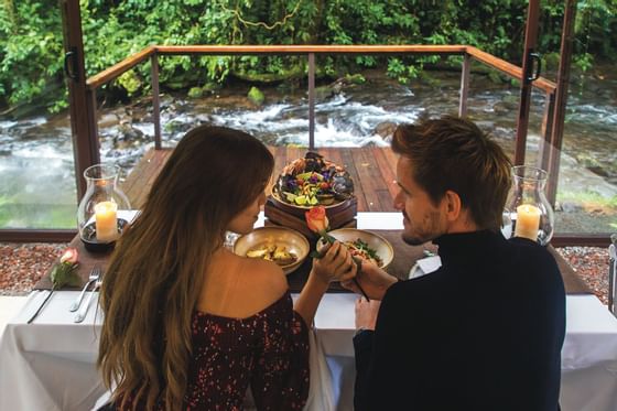 couple eating at dinner table in front of river