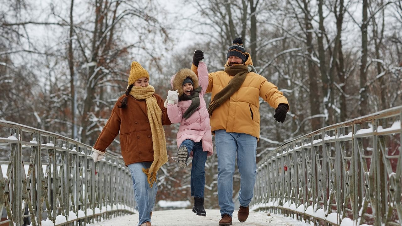 A family of four in winter clothes and hats is walking on a snowy bridge.