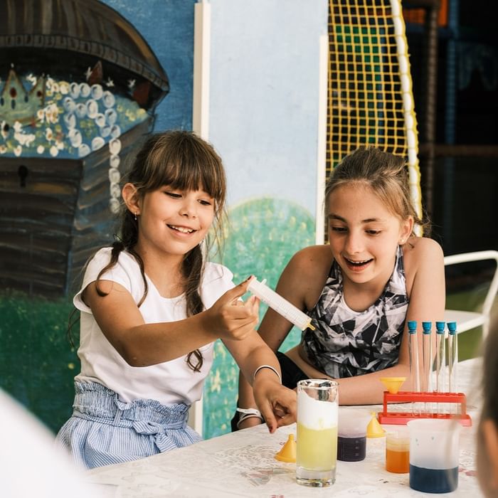 Dvije djevojčice provode eksperiment s kemijskom opremom na stolu.