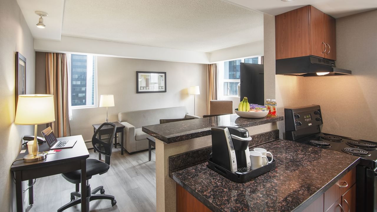 Hotel suite with work desk, chair, sofa, table, and kitchen area