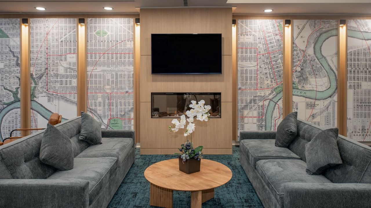 Hotel lobby area with gray couches, table, and city map wall decor in Campus Tower Suite Hotel.