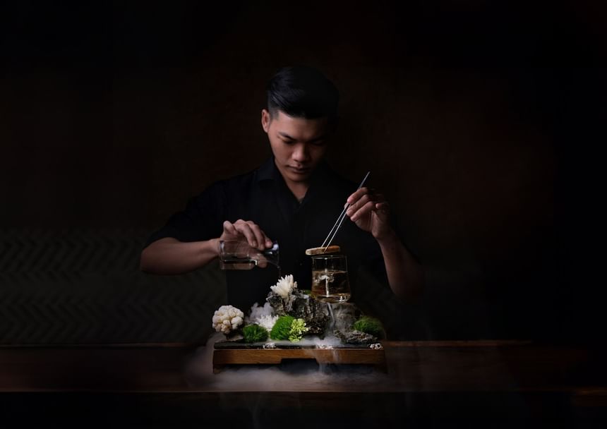 Bartender elegantly pouring liquid into a glass atop a rocky display in 2 Lam Son at Park Hyatt Saigon