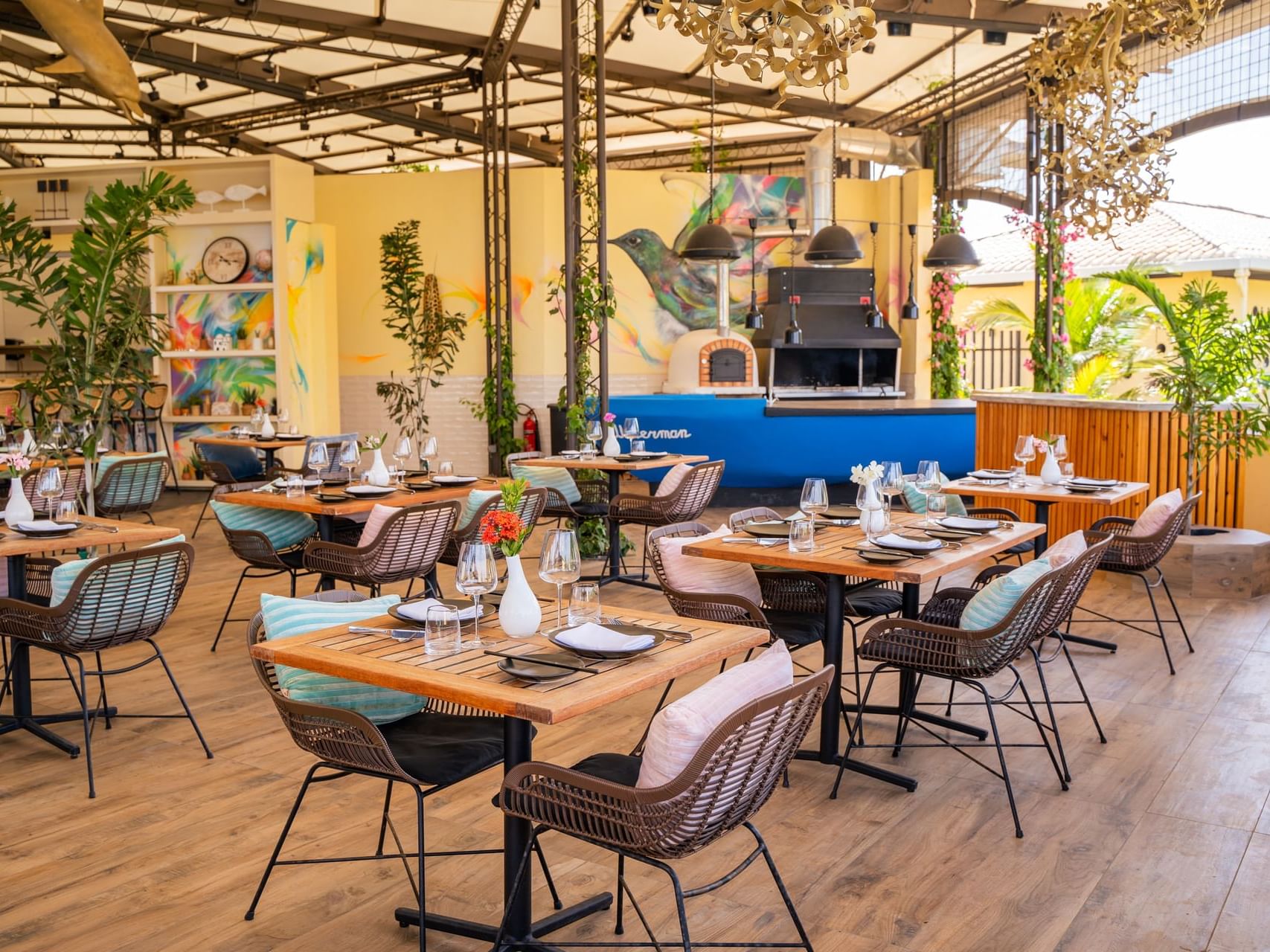 Eetgedeelte met tafels en gevlochten stoelen, gevuld met planten en decoratie in Bobbie’s Beach Club bij Golden Rock Resort