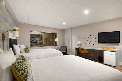 Modern Double Queen Handicap at The Riverwalk Plaza Hotel with two beds, desk, TV, window with city views, and warm lighting