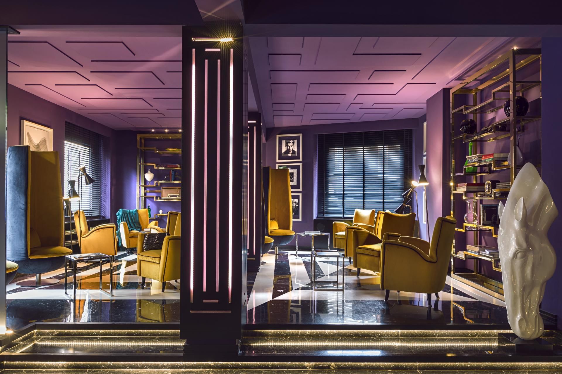 Lounge with purple walls, yellow armchairs, and stylish decor, illuminated by ambient lighting at The Tribune Hotel