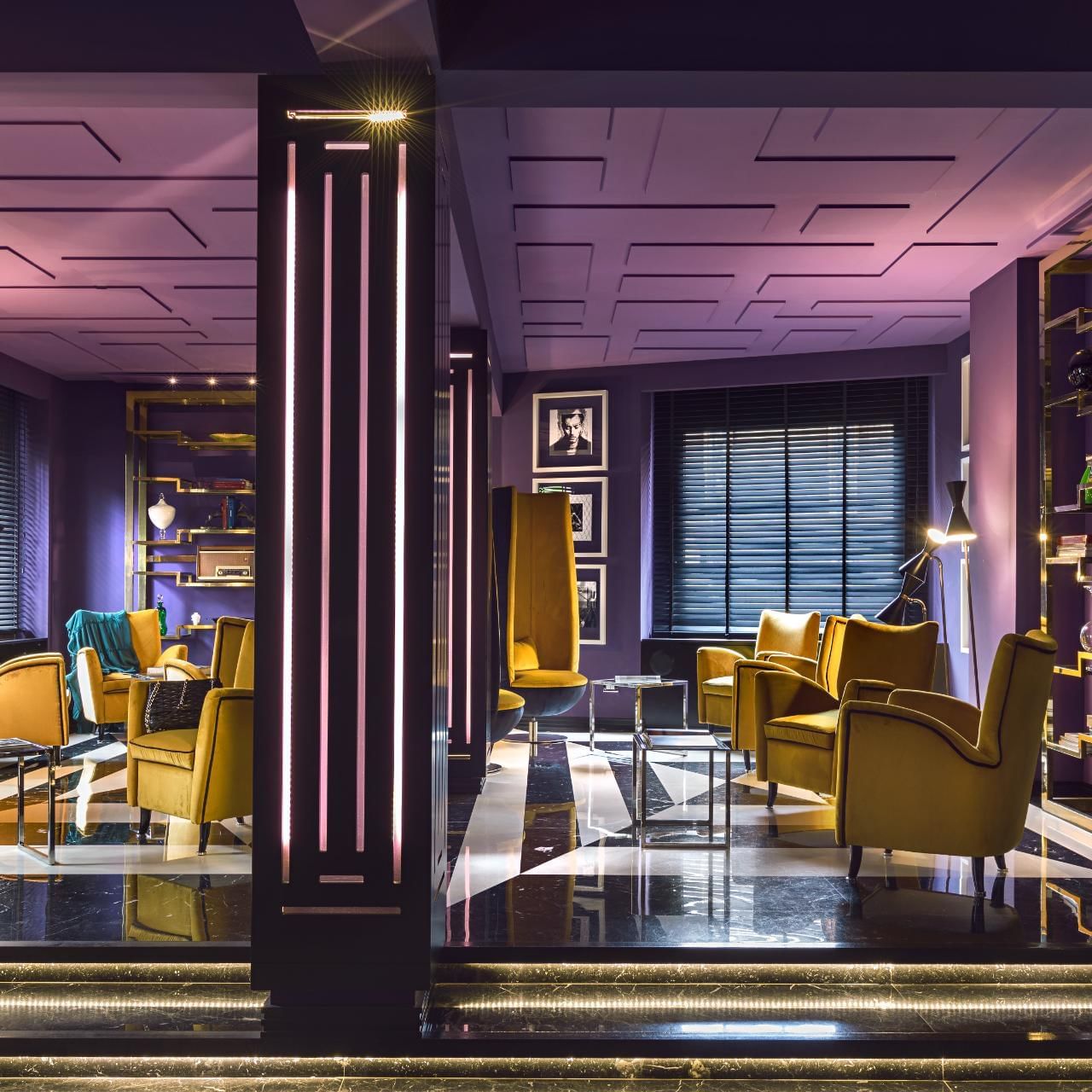 Lounge with purple walls, yellow armchairs, and stylish decor, illuminated by ambient lighting at The Tribune Hotel