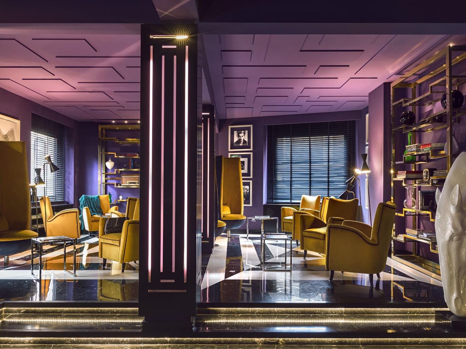 Lounge with purple walls, yellow armchairs, and stylish decor, illuminated by ambient lighting at The Tribune Hotel