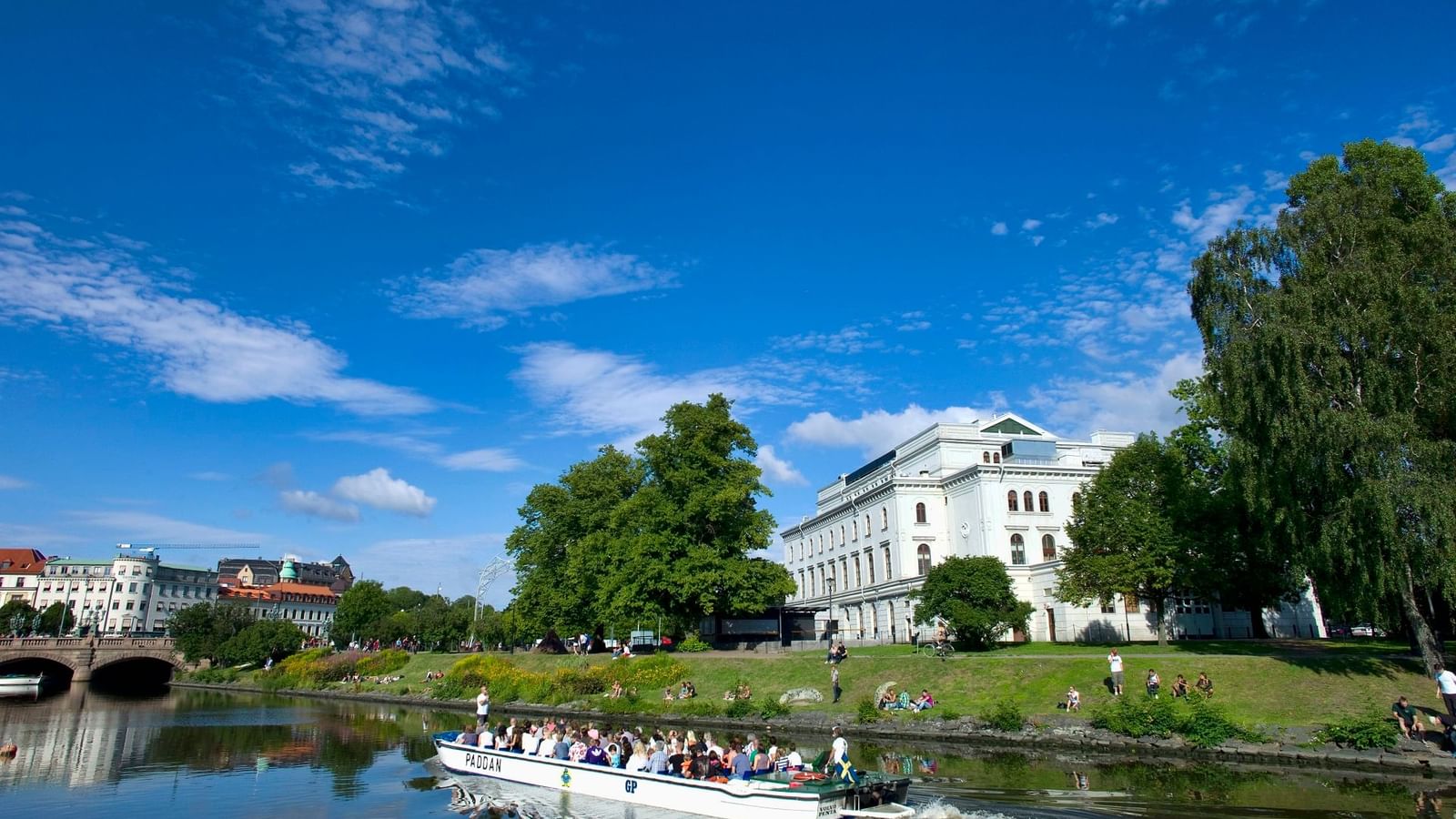 White boat moving on a canal with buildings and trees in Gothenburg, close to Hotel Riverton, Ideal for summer coolcation.