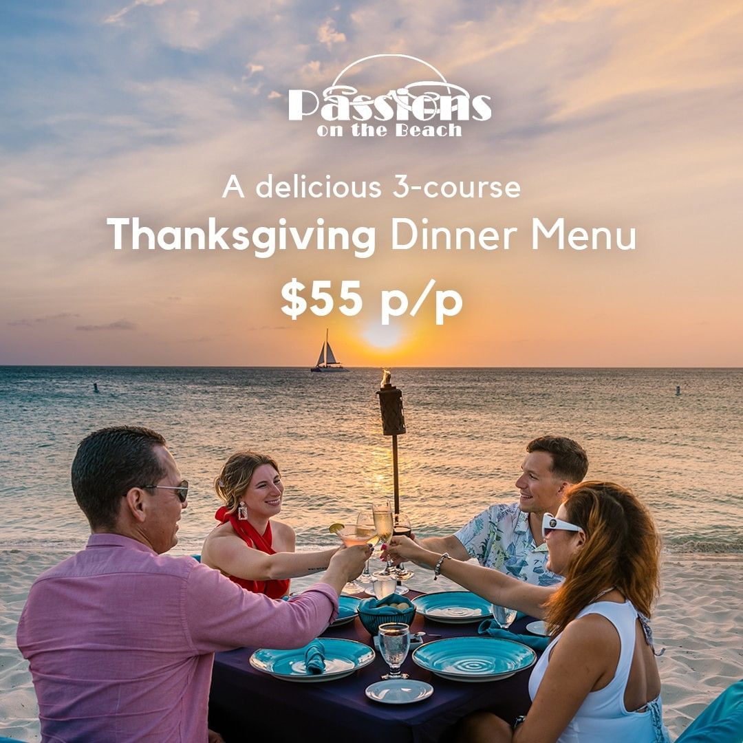 Family toasting at beachside table during sunset with sailboat in background for Thanksgiving dinner celebration.