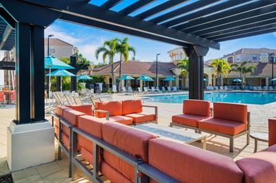 Orange lounge chairs and tables under a pergola near a pool at Vista Cay Resort By Millenium
