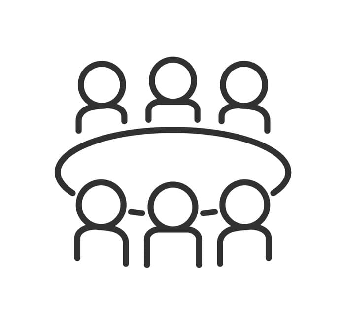 Six outlined figures sit around a circular table, illustrating a meeting or discussion group.