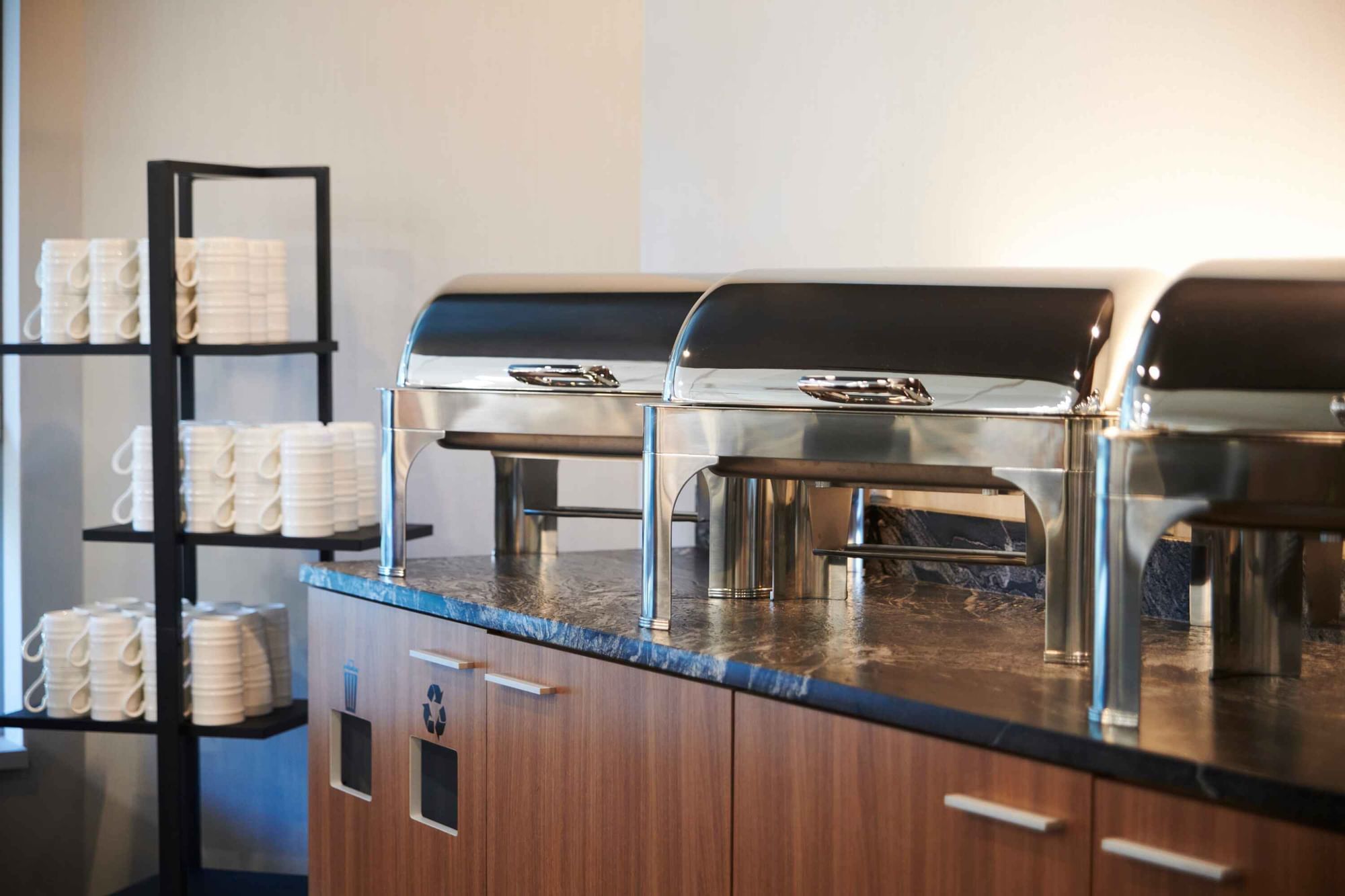 Breakfast buffet station at Warwick Hotels and Resorts with warm chafing dishes and a stack of coffee cups