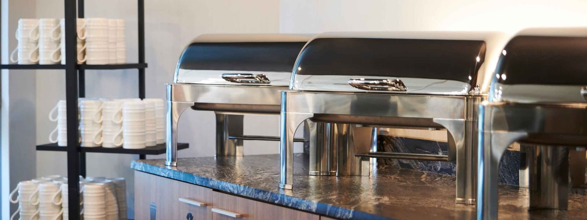 Buffet du petit-déjeuner dans les hôtels et complexes Warwick, avec des réchauds chauffants et une pile de tasses à café.