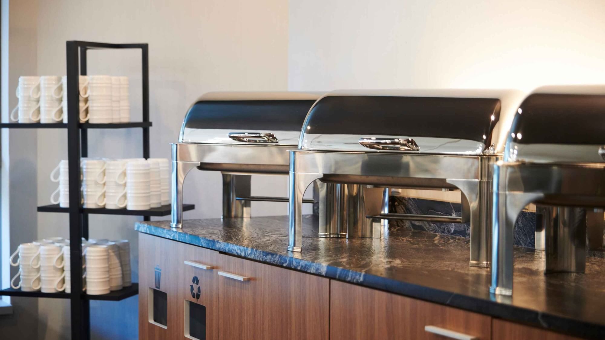 Breakfast buffet station at Warwick Hotels and Resorts with warm chafing dishes and a stack of coffee cups