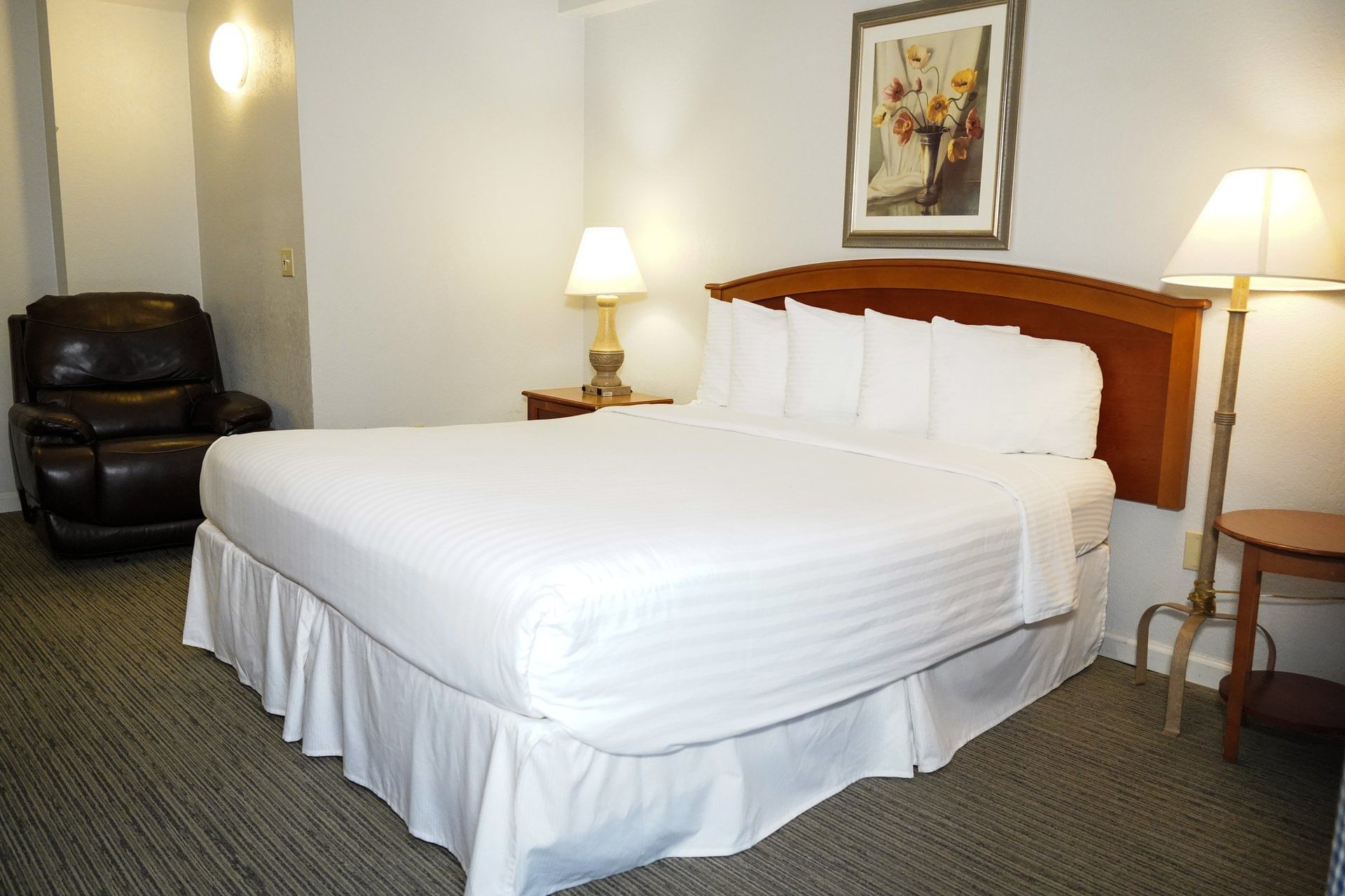 A standard hotel room with a large bed, leather armchair, and wooden nightstand.
