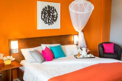 Bed with a coffee tray and colorful pillows by a black armchair under a canopy net in Superior Room at Hotel Montana Haiti