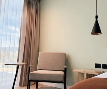Gray armchair by a large window with curtains & a black pendant light at Unika Hotels, a featured hotel in Bogota, Colombia