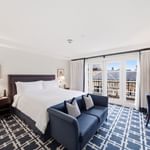 Bright hotel room with white bedding, navy sofa, geometric carpet, and balcony doors at el PRADO Hotel