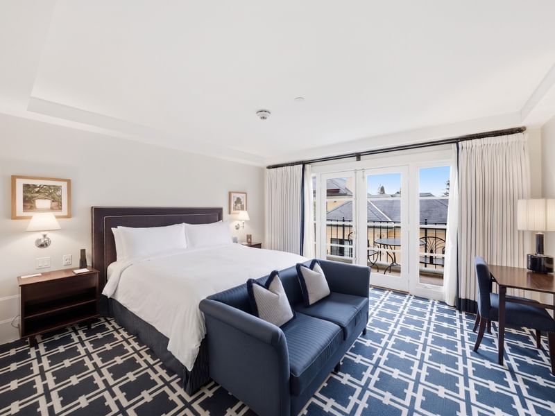 Deluxe King room with white bedding, navy sofa, patterned carpet, and balcony doors at el PRADO Hotel, Palo Alto.