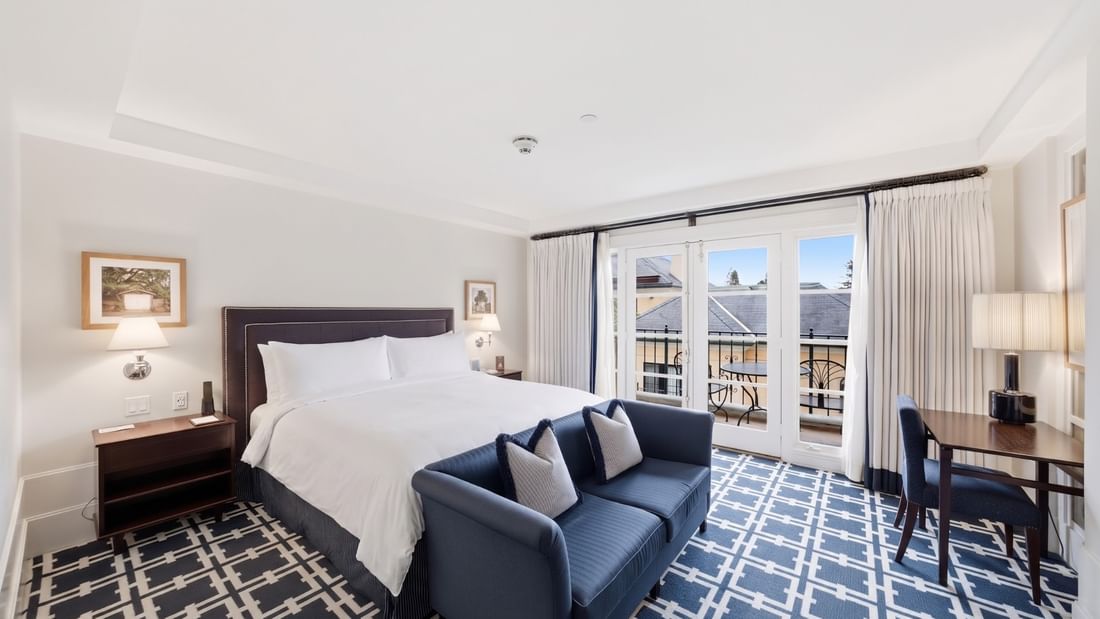 Deluxe King room with white bedding, navy sofa, patterned carpet, and balcony doors at el PRADO Hotel, Palo Alto.