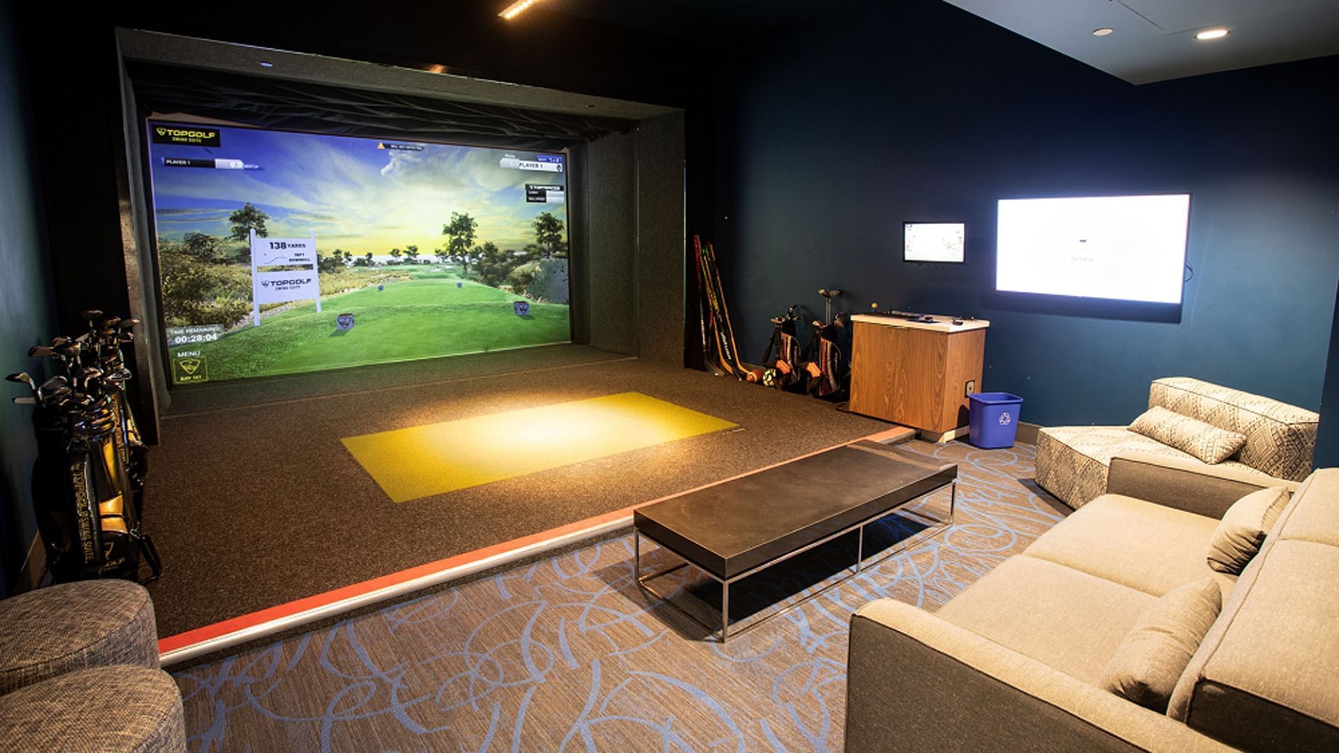 Topgolf Swing Suite featuring two screens with dark blue walls, a seating area, and golf clubs at Hotel X Toronto
