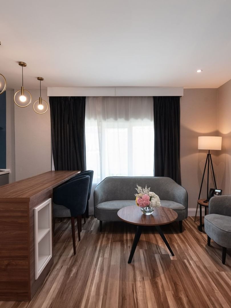 Grey sofa and armchair by a round coffee table near a wooden breakfast bar in Family Suite Sea View at Warwick Al Jubail