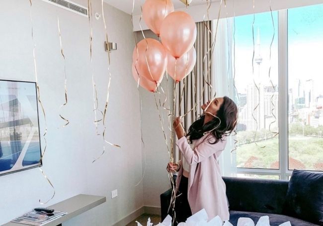 Person holding pink balloons in a room with city view outside the window at Hotel X Toront