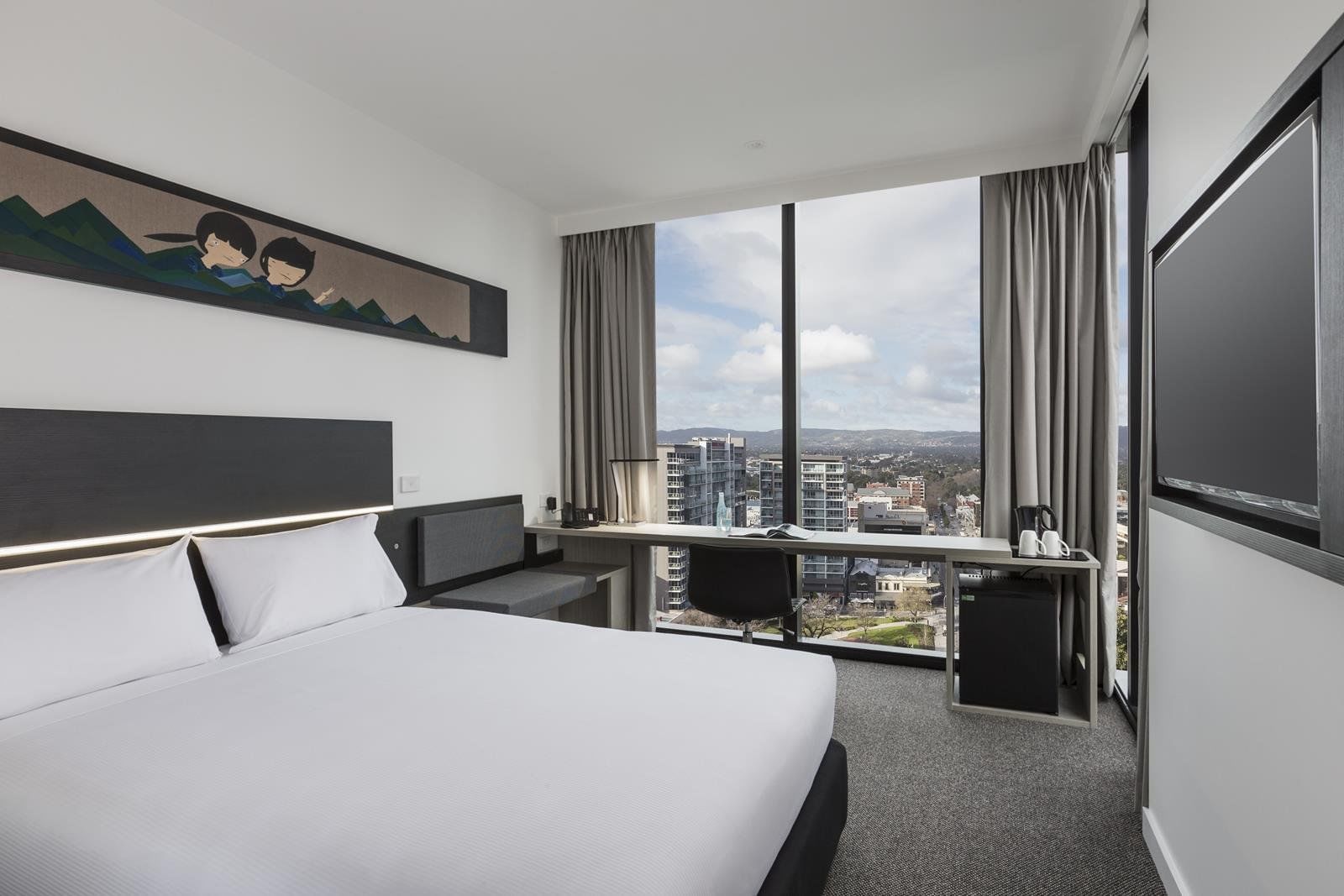 Bed and workspace by the large window offering city views in Superior view Queen Room at Ibis Adelaide