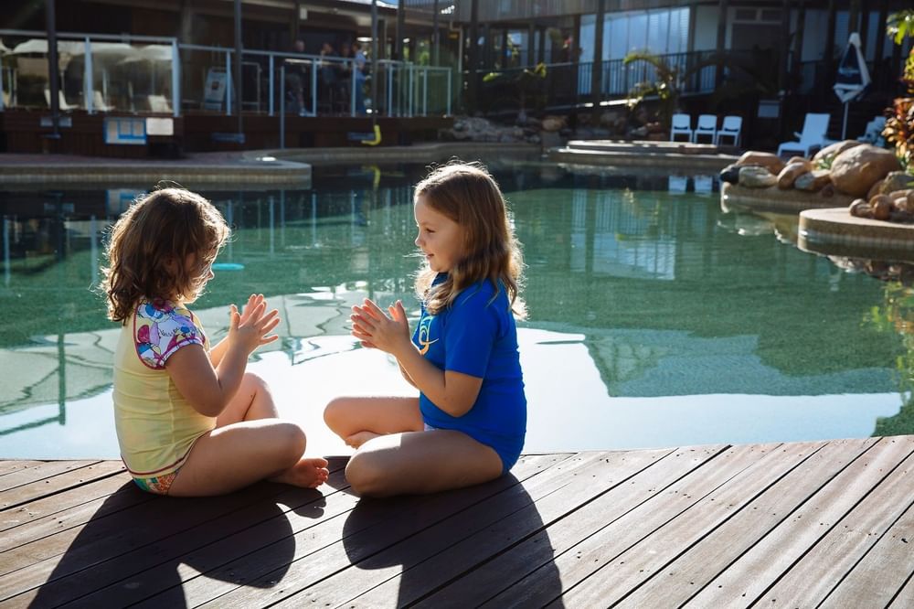 Joyful moment as two children play on the wooden poolside deck at Mercure Hotel Townsville, surrounded by tropical vibes
