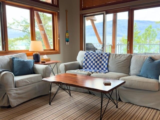 Bright living room with beige sofas, blue cushions, and large windows overlooking lake and mountains at Outback Lakeside Vacation Homes.
