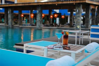 Colorful drinks sit on a table between two lounge chairs by the pool at Hotel Mykonos inviting guests to relax