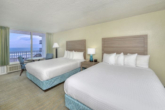 A hotel room with two beds, a desk, and a window with an ocean view.