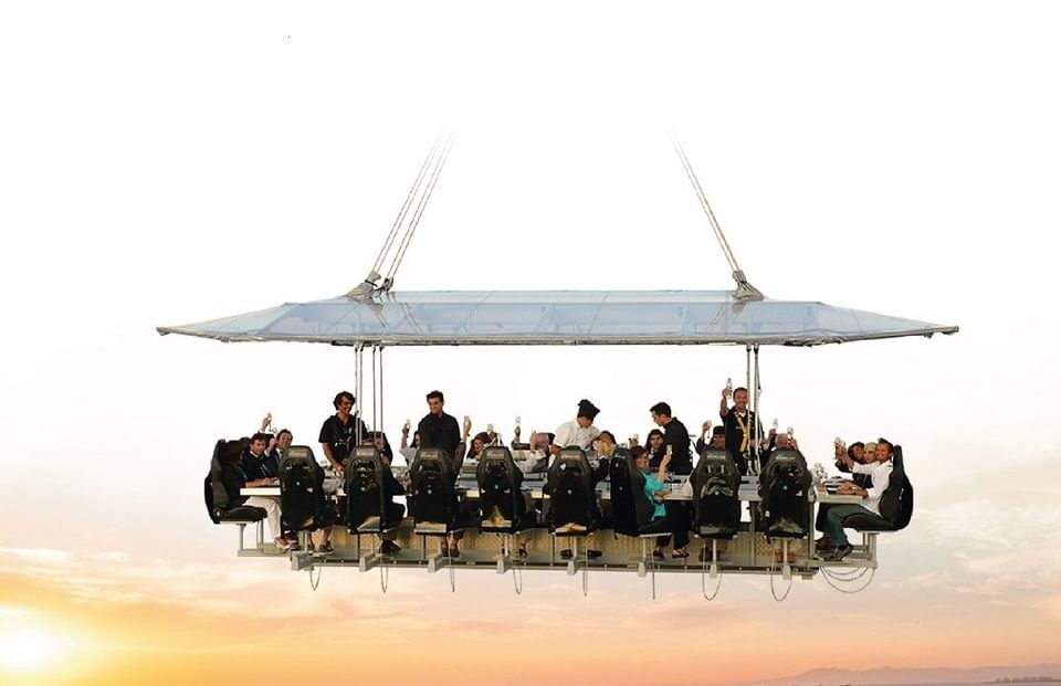 Guests enjoying a suspended dining table experience on an aerial platform during bright sunset at Hotel X Toronto