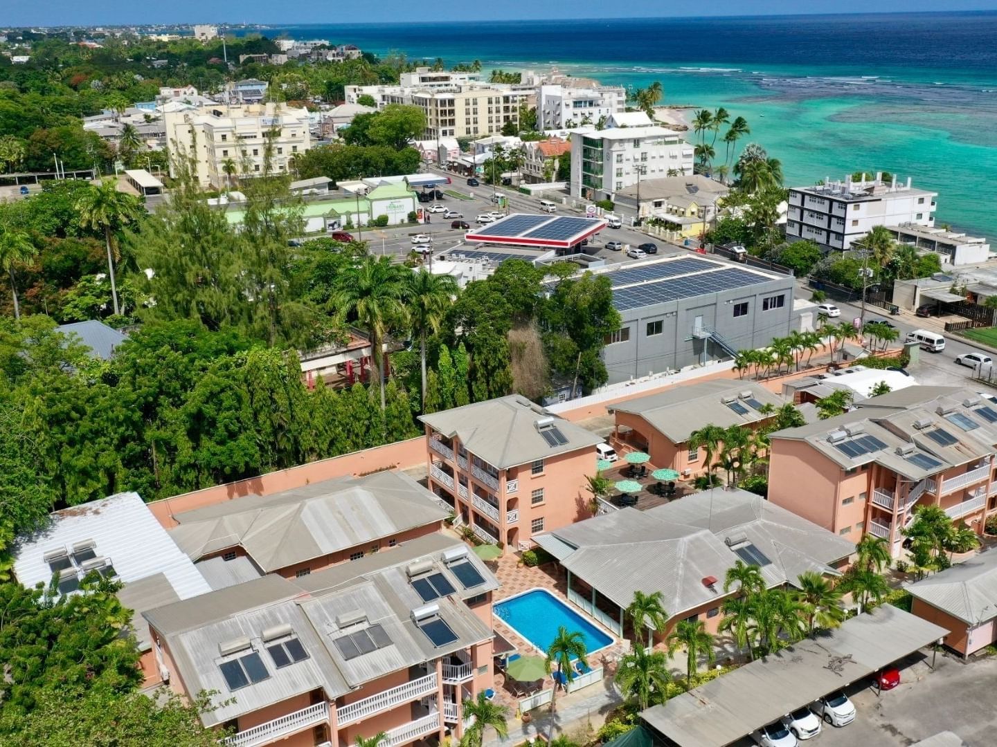 Aerial view of pink resort buildings with a swimming pool and tropical trees near the ocean at Worthing Court Apartment