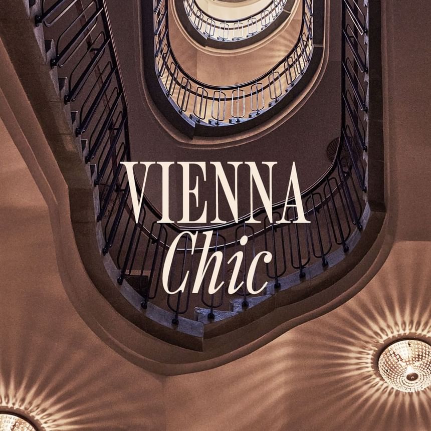 Vienna Chic banner featuring a spiral staircase with elegant railings and two ornate chandeliers at Hotel Motto Vienna