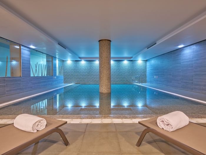 Two deckchairs with rolled-up towels by the side of the indoor swimming pool at Hotel Do Caracol