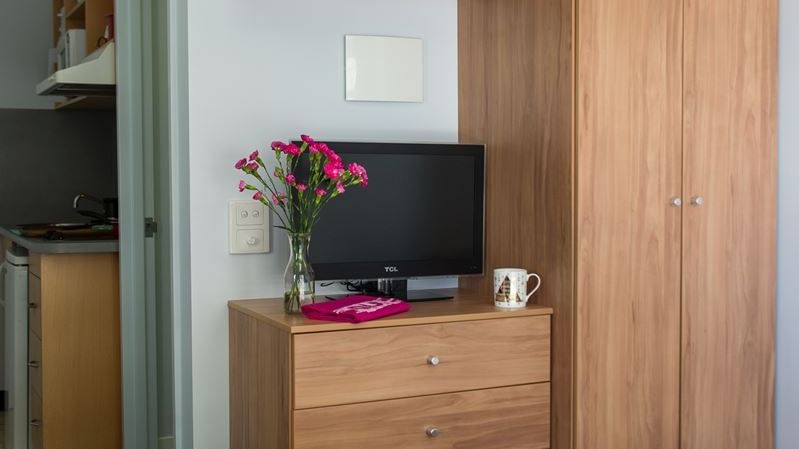 Compact student room with wooden wardrobe, dresser with TV, wall shelf, and turquoise bedding at StudentLiving - on Margaret