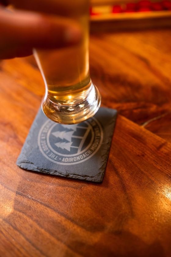 Hand holding a glass of beer on a wooden table in The Lodge at Schroon Lake