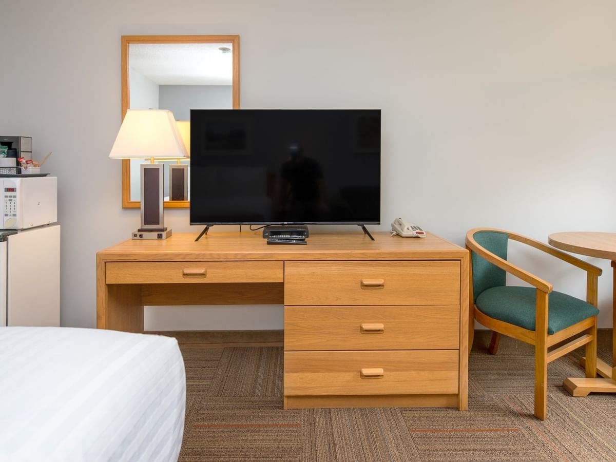 Hotel room with bed, desk with TV and lamp, microwave, mini-fridge, table, and two chairs.