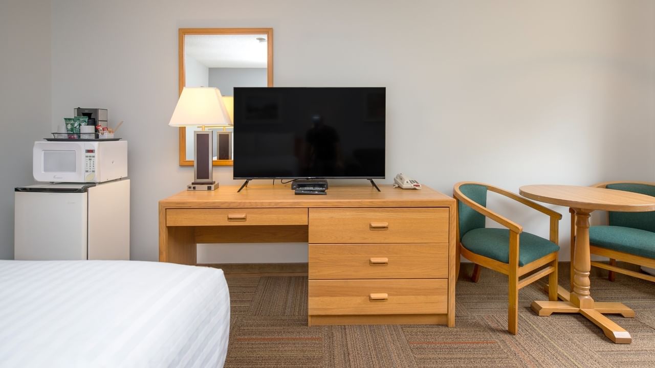 Hotel room with bed, desk with TV and lamp, microwave, mini-fridge, table, and two chairs.